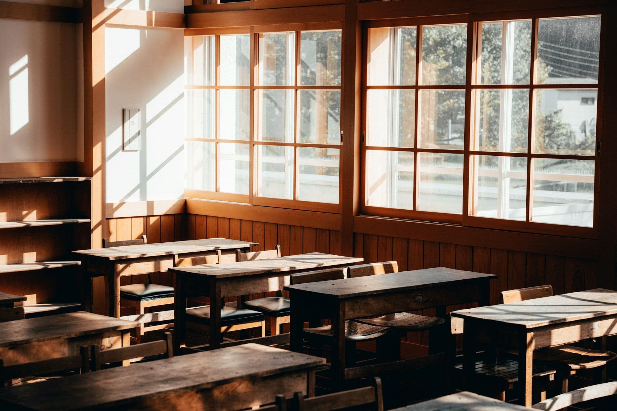 Sunlit classroom with wooden desks and tall windows